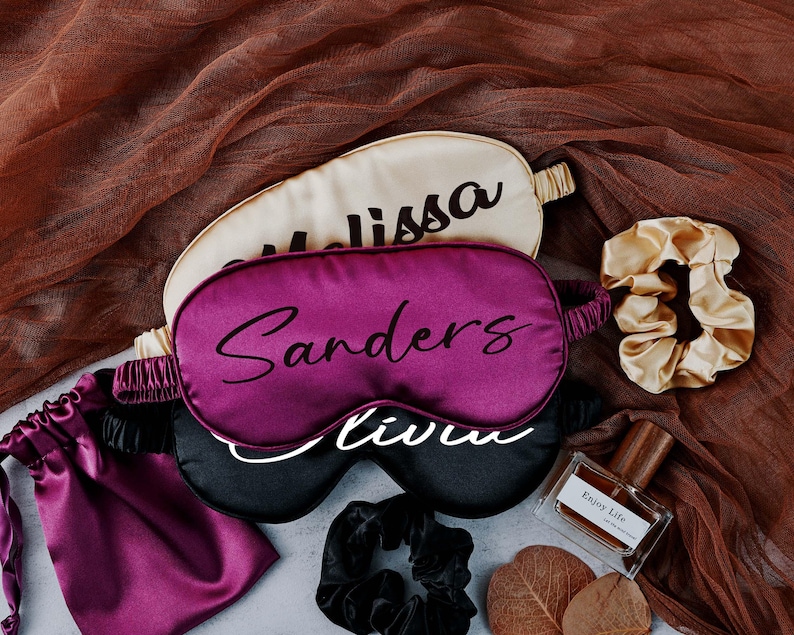 May include: Three satin sleep masks with personalised names, "Melissa", "Sanders", and "Olivia",  along with a small bottle of perfume labelled "Enjoy Life" and two hair scrunchies.