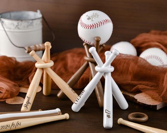 May include: Wooden baseball bat-shaped holders, some with white paint, are arranged with baseballs. One baseball is on a wooden stand. Some bats have text: "Respect", "#17", and "2024/9/14". A small white bucket is in the background.