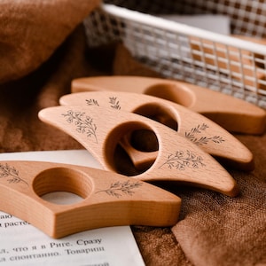 May include: Four wooden thumb page holders with floral designs are arranged on a brown surface. The light-colored wood has a smooth finish. A white basket and a piece of paper with text are in the background. The page holders are for books.