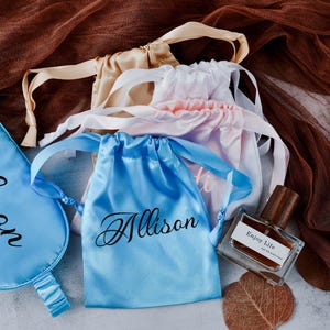May include: A set of three blue satin sleep masks and a small blue satin drawstring bag with the name "Allison" embroidered on each. A small bottle of perfume with the text "Enjoy Life" is also included.