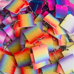 Peut inclure: Un tas d'étiquettes carrées colorées avec des chaînes à billes argentées. Les étiquettes présentent un dégradé de couleurs, notamment rouge, orange, jaune, vert, bleu et violet. Certains ont des cercles ou des lignes superposés.