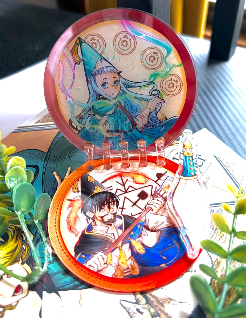 May include: A circular, hinged acrylic display piece featuring two distinct illustrations. The top disc shows a character in a blue pointed hat with magical symbols, while the bottom disc depicts a bearded character holding a staff with fire effects.