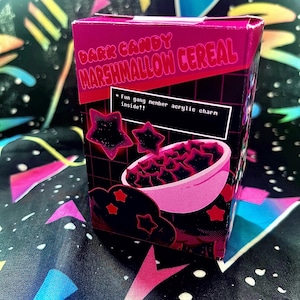 May include: A box of "Dark Candy Marshmallow Cereal" with a pink and black design. The box features a bowl of star-shaped marshmallows and the text "Fun gang member acrylic charm inside!!". The background has a colorful, space-themed pattern.