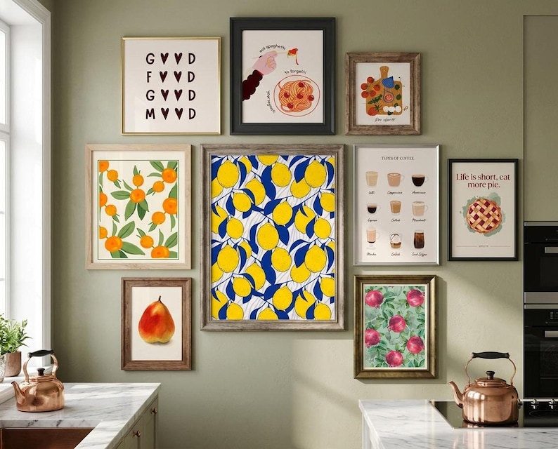A gallery wall displaying nine framed kitchen-themed art prints including lemons, coffee, pomegranates, and pie against a pale green wall above a kitchen counter.