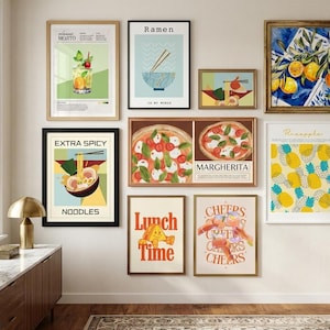 A gallery wall showcasing ten framed food and beverage art prints including pizza, ramen, cocktails, and pineapples above a wooden cabinet.