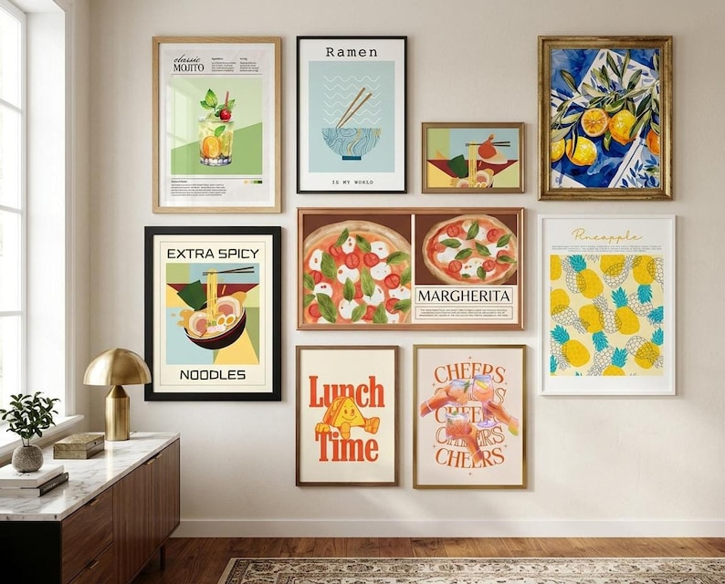 A gallery wall showcasing ten framed food and beverage art prints including pizza, ramen, cocktails, and pineapples above a wooden cabinet.