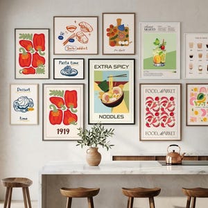 A gallery wall arrangement of ten food prints featuring ramen, sushi, peppers, and cocktails above a kitchen island with bar stools.