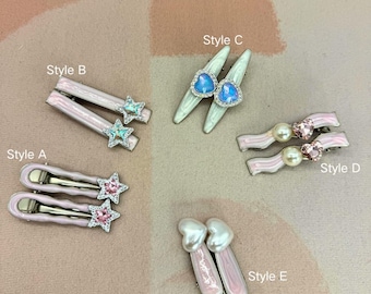 May include: A collection of hair clips in various styles. Styles include pink and silver barrettes with star and heart accents, and clips with pearl and crystal embellishments. The clips are displayed on a neutral surface.