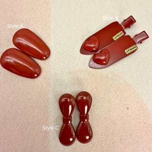 Peut inclure: Collection de trois styles d'accessoires capillaires bordeaux. Le style A comprend deux pinces ovales. Le style B présente deux pinces avec des cœurs et le texte "LOVEDAYS". Le style C montre deux boucles d'oreilles en forme de goutte.