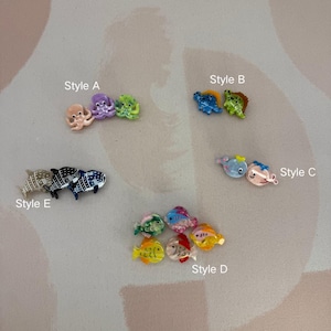Op de afbeelding: Een verzameling kleurrijke, miniatuur bedels met oceaanthema. Stijlen omvatten octopussen, dinosaurussen, walvissen en verschillende vissen. Elke bedel is helder gekleurd met gedetailleerde ontwerpen, perfect voor knutselen of sieraden.