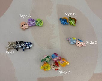 May include: A collection of colorful, miniature ocean-themed charms. Styles include octopuses, dinosaurs, whales, and various fish. Each charm is brightly colored with detailed designs, perfect for crafting or jewelry making.