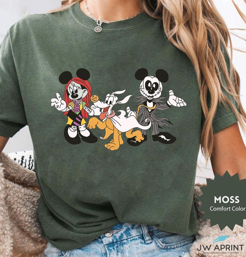 Puede incluir: Camiseta verde musgo de color c&oacute;modo con un gr&aacute;fico de dibujos animados de tres personajes. Los personajes son una ratona con pelo rojo, un perro y un rat&oacute;n esqueleto. La camiseta tiene el texto "MOSS Comfort Color" en la esquina inferior derecha.