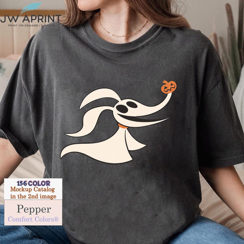 Puede incluir: Camiseta gris oscuro con un personaje de perro fantasma de dibujos animados sosteniendo una calabaza. La camiseta tiene el texto "JW APRINT" en la parte superior y "Pepper Comfort Colors&reg;" en la parte inferior. La camiseta es de la marca Comfort Colors.