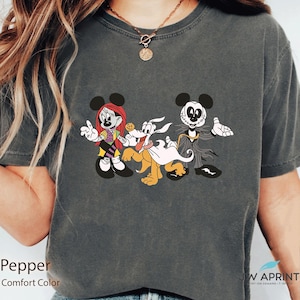 Puede incluir: Camiseta gris oscuro con un dise&ntilde;o de dibujos animados con tem&aacute;tica de Halloween. El dise&ntilde;o incluye un personaje de rat&oacute;n femenino con pelo rojo, un perro y un personaje de rat&oacute;n masculino con traje. La camiseta est&aacute; etiquetada como "Pepper" y "Comfort Color".