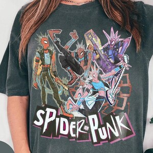 May include: Dark gray t-shirt featuring a colorful graphic of Spider-Man characters playing musical instruments. The design includes the text "SPIDER-PUNK" in a stylized font, with a punk rock aesthetic.