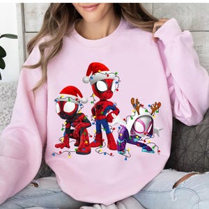 Peut inclure: Un sweat-shirt rose clair avec trois personnages de Spider-Man en tenues de No&euml;l. Les personnages portent des bonnets de P&egrave;re No&euml;l et des bois de rennes, et sont d&eacute;cor&eacute;s de guirlandes lumineuses color&eacute;es.