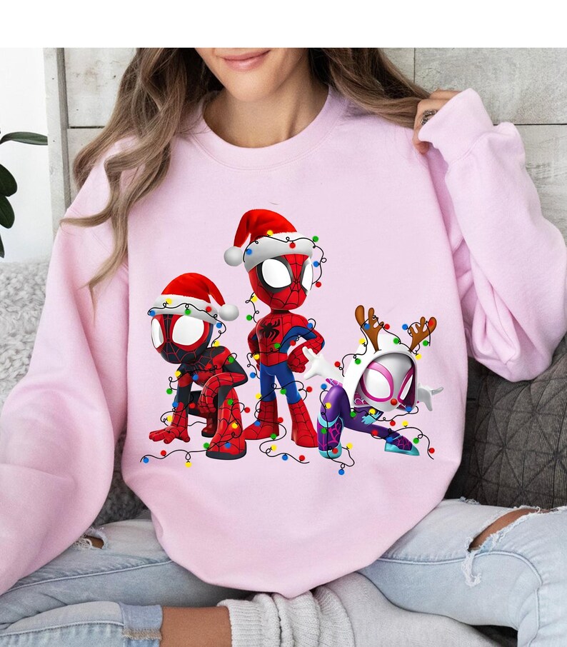 Peut inclure: Un sweat-shirt rose clair avec trois personnages de Spider-Man en tenues de No&euml;l. Les personnages portent des bonnets de P&egrave;re No&euml;l et des bois de rennes, et sont d&eacute;cor&eacute;s de guirlandes lumineuses color&eacute;es.