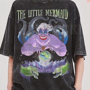 May include: Black t-shirt featuring a graphic of Ursula from The Little Mermaid. The design includes Ursula, tentacles, and the text "THE LITTLE MERMAID". The artwork is in shades of purple, green, and blue.
