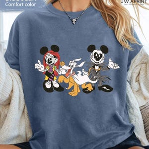 Puede incluir: Camiseta azul vaquero de color c&oacute;modo con un gr&aacute;fico de personajes de dibujos animados. El dise&ntilde;o incluye a Minnie Mouse, Pluto y Jack Skellington. La camiseta es de color azul liso.
