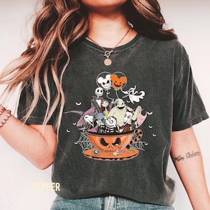 May include: Dark gray t-shirt featuring a Halloween-themed design. The graphic shows characters from The Nightmare Before Christmas inside a jack-o'-lantern teacup. Includes orange and white balloons, a spider web, and the word "Pepper" at the bottom.