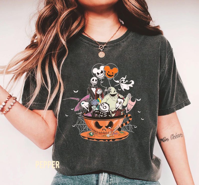 May include: Dark gray t-shirt featuring a Halloween-themed design. The graphic shows characters from The Nightmare Before Christmas inside a jack-o'-lantern teacup. Includes orange and white balloons, a spider web, and the word "Pepper" at the bottom.