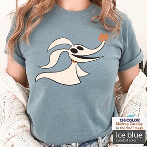 Puede incluir: Camiseta azul hielo de color c&oacute;modo con un personaje de perro fantasma de dibujos animados con una nariz de calabaza. El gr&aacute;fico es en negro, blanco y naranja. La camiseta tiene las mangas enrolladas.