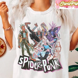 May include: White t-shirt featuring a colorful graphic of Spider-Man characters in punk rock attire. The design includes the text "SPIDER-PUNK" in a bold, stylized font. The image showcases a vibrant, comic book style illustration.
