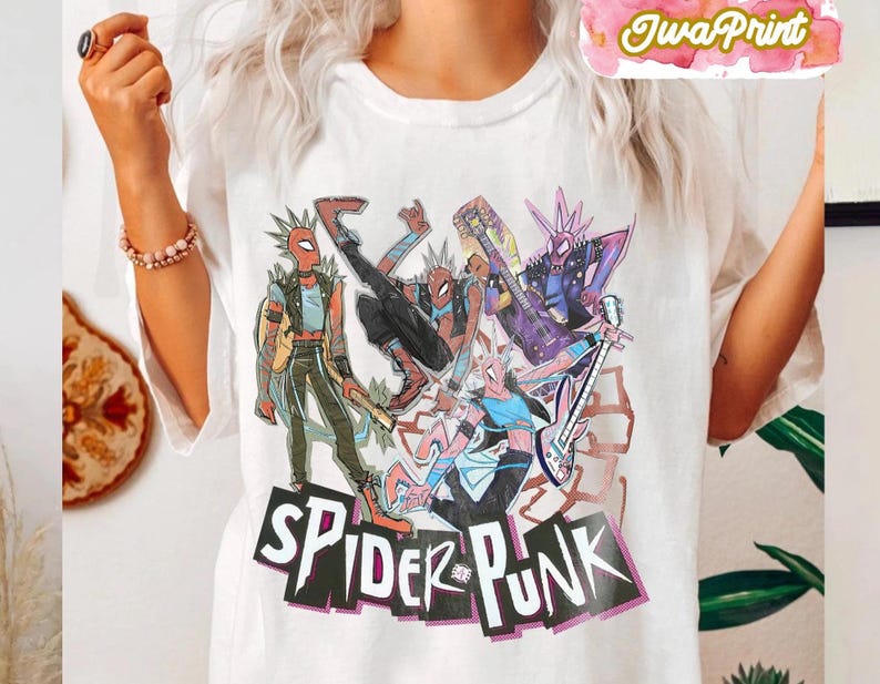 May include: White t-shirt featuring a colorful graphic of Spider-Man characters in punk rock attire. The design includes the text "SPIDER-PUNK" in a bold, stylized font. The image showcases a vibrant, comic book style illustration.