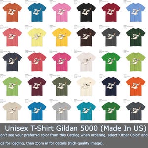Puede incluir: Una variedad de camisetas unisex Gildan 5000 en varios colores, cada una con un gr&aacute;fico blanco de un personaje con una nariz larga y un coraz&oacute;n peque&ntilde;o. Las camisetas se muestran en una cuadr&iacute;cula, con el texto "Unisex T-Shirt Gildan 5000 (Made In US)" en la parte inferior.