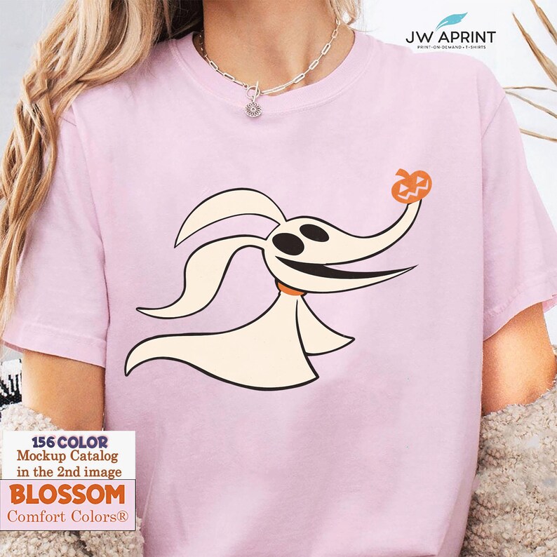 Puede incluir: Una camiseta rosa claro con un perro fantasma de dibujos animados sosteniendo una calabaza. El perro fantasma es blanco con detalles negros y un collar naranja. La camiseta tambi&eacute;n tiene el texto "JW APRINT" y "BLOSSOM Comfort Colors&reg;".
