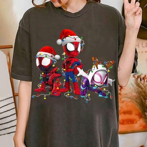 Peut inclure: T-shirt gris fonc&eacute; avec trois personnages de Spider-Man en tenue de No&euml;l. Les personnages portent des bonnets de P&egrave;re No&euml;l et sont entour&eacute;s de guirlandes lumineuses color&eacute;es. Un personnage porte des bois de renne.