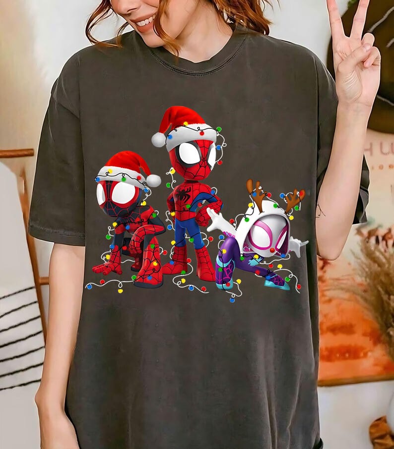 Peut inclure: T-shirt gris fonc&eacute; avec trois personnages de Spider-Man en tenue de No&euml;l. Les personnages portent des bonnets de P&egrave;re No&euml;l et sont entour&eacute;s de guirlandes lumineuses color&eacute;es. Un personnage porte des bois de renne.