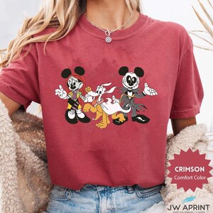 Puede incluir: Camiseta Crimson Comfort Color con un dibujo animado de Minnie Mouse, Pluto y Jack Skellington con tem&aacute;tica de Halloween. La camiseta tiene el texto "CRIMSON Comfort Color" y "JW APRINT" impreso.
