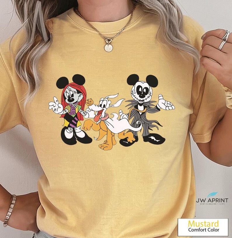 Puede incluir: Camiseta de color mostaza con un gr&aacute;fico de dibujos animados de Minnie Mouse, Pluto y Jack Skellington. Minnie lleva una peluca roja y un atuendo morado y negro. Pluto tiene una s&aacute;bana blanca. Jack lleva un traje negro y gris.