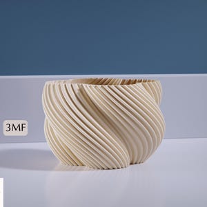 Op de afbeelding: Een witte keramische plantenpot met een draaiend, geribbeld ontwerp. De pot heeft een moderne, organische vorm.