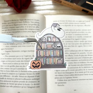 Peut inclure: Marque-page fantaisiste avec un fantôme portant un livre sur la tête, assis sur une étagère. L'étagère est ornée d'éléments d'Halloween, dont une citrouille et des toiles d'araignées. Le marque-page est dans un livre ouvert.
