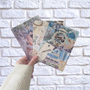 Könnte beinhalten: Drei dekorative Postkarten im Vintage-Stil werden in einer Hand gehalten. Die Postkarten zeigen florale, Uhren- und architektonische Elemente in Pastellfarben. Der Hintergrund ist eine weiße Backsteinmauer.