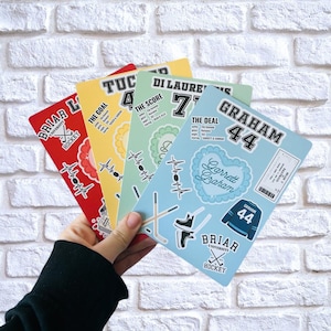Peut inclure: Quatre carnets sur le thème du hockey, rouges, jaunes, verts et bleus, sont tenus dans une main. Chaque carnet présente du texte et des graphiques différents, notamment des crosses de hockey, des patins et le texte "Briar University Hockey."