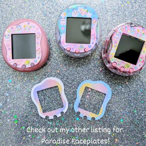 May include: Three colorful handheld digital pet devices with screens, in pink, clear, and pink. Two matching faceplates are below. The devices have decorative patterns and buttons. Text at the bottom reads "Check out my other listing for Paradise Faceplates!"