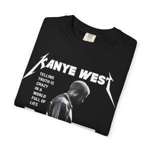 May include: Black t-shirt featuring the text "Kanye West" in a stylized font, with an image of Kanye West. The shirt also includes the quote "Telling truth is crazy in a world full of lies."