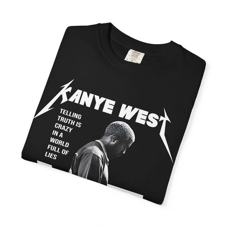 May include: Black t-shirt featuring the text "Kanye West" in a stylized font, with an image of Kanye West. The shirt also includes the quote "Telling truth is crazy in a world full of lies."