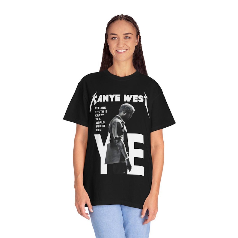 May include: Black t-shirt featuring the text "Kanye West" in white, with a black and white image of a person. The text "Telling truth is crazy in a world full of lies" is also printed on the shirt. The word "YE" is printed in large white letters.