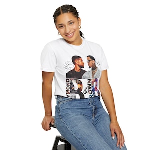 K&ouml;nnte beinhalten: Wei&szlig;es T-Shirt mit einer Grafik von zwei M&auml;nnern, Unterschriften und dem Text "Raymond & Brown". Die Person tr&auml;gt eine blaue Jeans. Das Design enth&auml;lt die W&ouml;rter "Raymond" und "Brown" in einer stilisierten Schriftart.
