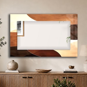 May include: A rectangular wall mirror featuring a decorative border with abstract, layered shapes in shades of cream, tan, and dark brown. The mirror has a clear, reflective centre panel and is mounted horizontally on a plain, light-coloured wall.