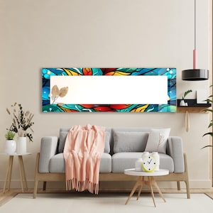 May include: A long rectangular mirror with a colorful abstract design featuring blue, red, yellow, and orange hues. The mirror is hanging on a wall above a gray sofa with a throw blanket and a small round table.