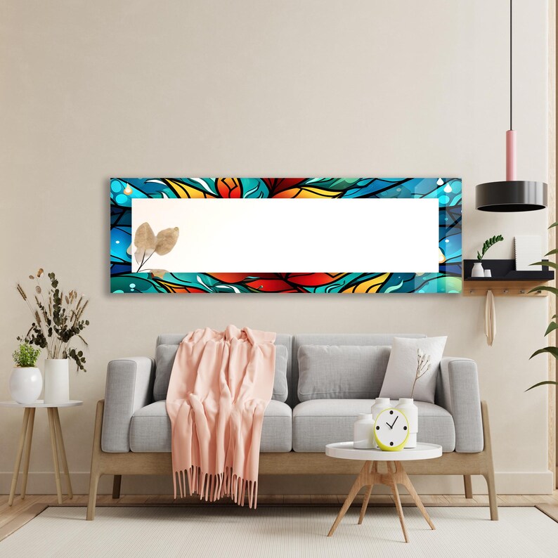 May include: A long rectangular mirror with a colorful abstract design featuring blue, red, yellow, and orange hues. The mirror is hanging on a wall above a gray sofa with a throw blanket and a small round table.