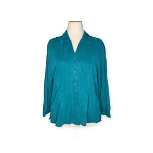 May include: Teal-colored button-down shirt with long sleeves. The shirt has a V-neck collar and is displayed on a mannequin. The fabric appears to have a subtle texture. The shirt is a solid color and has a classic design.