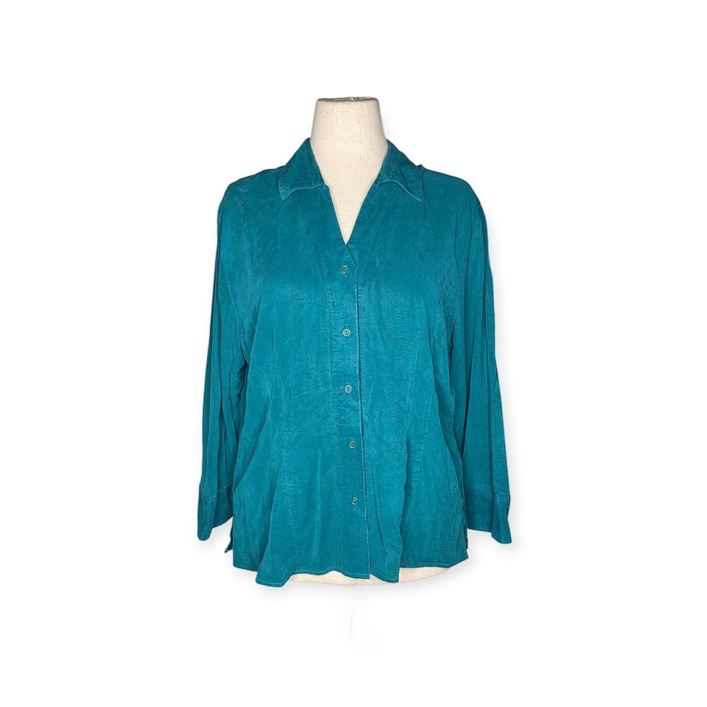 May include: Teal-colored button-down shirt with long sleeves. The shirt has a V-neck collar and is displayed on a mannequin. The fabric appears to have a subtle texture. The shirt is a solid color and has a classic design.
