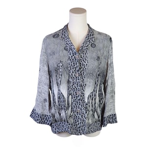 Op de afbeelding: Een button-down shirt met een grijze en zwarte giraffenprint. De blouse heeft een kraag, lange mouwen en een knoopsluiting. De manchetten en kraag hebben een stippenpatroon. De blouse wordt op een mannequin gepresenteerd.