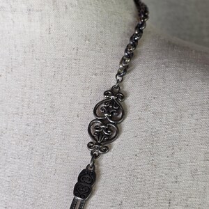 May include: A silver necklace with an elaborate, filigree design. The necklace has a chain, decorative centrepieces, and a tassel-like drop. The intricate details and vintage style create a classic look.